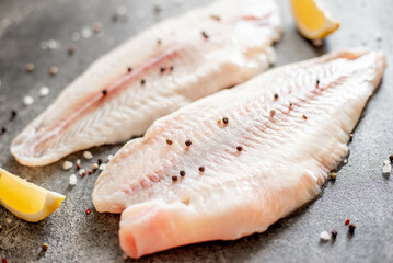 Wall Mural - Fresh raw white fish fillet Pangasius with spices and lemon on a stone background.