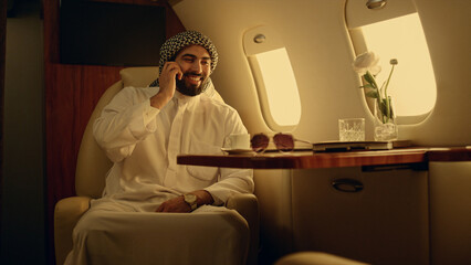 Wall Mural - Millionaire talking cell phone in airplane. Happy arabian man picking call