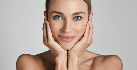 skin care. beautiful woman with healthy facial skin touching hands moisturized face skin, on light g