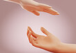 © Kyrylo Ryzhov - Two hands reaching on another over pink background. Concept of support, care, love, protection and connection between people. 3D rendering.
