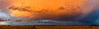 Panoramafoto einer abziehenden Gewitterwolke, die vom Licht der untergehenden Sonne orange angestrahlt wird