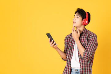 Wall Mural - Smile happy asian man wearing scottish shirt with jeans isolated on yellow background using smartphone and headphone looking at copy space