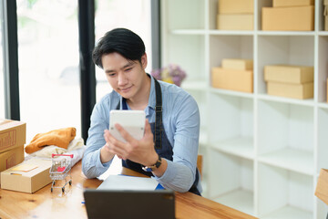 A portrait of .a small start-up and an SME owner, an Asian male entrepreneur using a calculator to calculate profits from selling products online