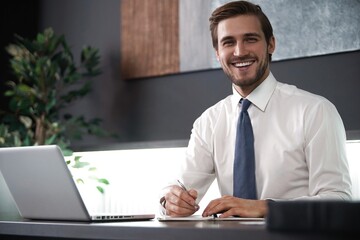 Wall Mural - Portrait of young smiling man sitting at his desk in the office.