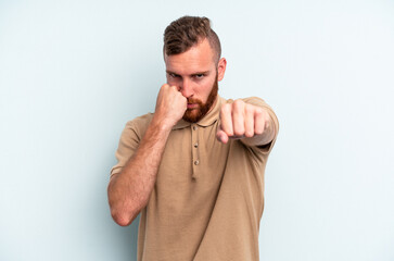 Young caucasian man isolated on blue background throwing a punch, anger, fighting due to an argument, boxing.