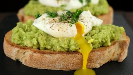 Wall Mural - Avocado toast with poached egg close up. Cutting poached egg with runny egg yolk over bread toast with mashed avocado spread