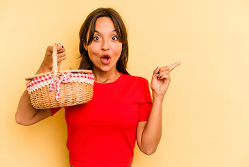 Wall Mural - Young hispanic woman going to do it picnic isolated on yellow background pointing to the side