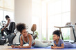 © bigy9950 - African American mother and daughter in sportswear practicing yoga together on yoga mat at the gym. Black family sporty fitness workout.