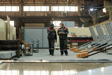 Poster - Two young intercultural male workers of factory having discussion of working points while moving along spacious workshop