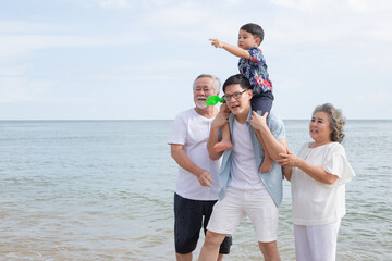 Asian family walking on the beach together. son sitting on father's shoulder with support from grandmother and grandfather. travel vacation on summer