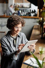 Poster - Smiling businesswoman, owner of cafe or restaurant, looking through online orders of clients while scrolling on tablet screen