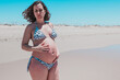 Pregnant woman on the beach. Adult lady on the beach about to give birth. High risk pregnancy. Miss shows the belly of her 8-month-old unborn baby.