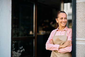 Happy flower shop owner standing with her arms crossed and looking away,