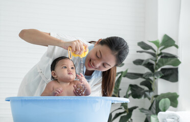 selective focus on asian young mother hand holding sponge and squeeze water to drop on her little ba