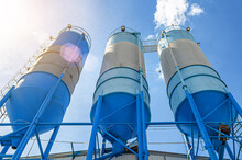 Large Blue Industrial Tanks For Cement, Sand, Water. Blue Sky Background With White Clouds.