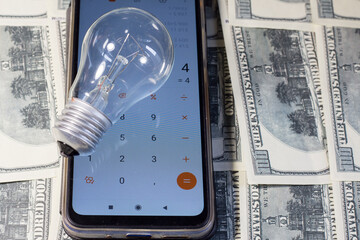 Wall Mural - A light bulb lay on a calculator and banknotes. Saving electricity in Ukraine due to the war