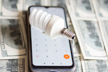 Wall Mural - A fluorescent light bulb lay on a calculator and banknotes. Saving electricity in Ukraine due to the war