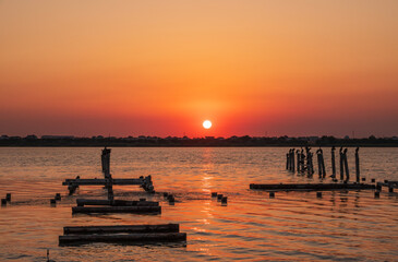 Beautiful red and orange sunset over the sea. The sun goes down over the sea. A flock of cormorants sits on a old sea pier in orange sunset light