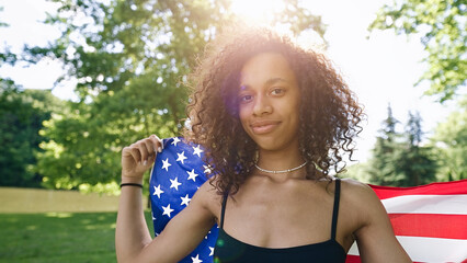 Young African american woman is waving American flag on top of at nature background. USA resident, US citizen. Immigration concept