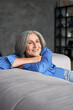 © insta_photos - Smiling relaxed mature old woman resting dreaming sitting on couch at home. Happy mid aged woman relaxing. Peaceful serene grey-haired lady feeling peace of mind, no stress on sofa, vertical view.