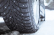 Close up of car winter tire with metal spikes in cold snow conditions, View from the ground. Shallow depth of field.