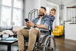 © sofiko14 - Happy son unexpectedly closing father's eyes from back in modern living room. School boy surprising disabled dad in wheelchair with smartphone in hands.