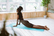 © Юля Бурмистрова - Rearview of relaxing dark skin african american woman in black outfit doing exercises, practising yoga on mat at home. Stretching in cobra asana pose, Bhujangasana near window. Health and body care