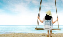 Asian Woman In Casual Style Wear Hat And Sandals Sit On Swings At Sand Beach  And Looking Beautiful Tropical Paradise Sea And Sky. Summer Vacation. Summer Vibes. Enjoying And Relaxing Girl On Holiday.