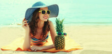Summer Portrait Of Happy Smiling Young Woman Lying On The Beach With Funny Pineapple Wearing Straw Hat