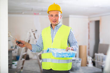 Wall Mural - Cheerful man construction worker holding paint roller and tray. Painting wall in apartment, home improvement works.