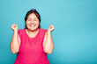 © Lux Images - Cheerful curvy Latin woman with a wide smile and clenched fists, isolated on blue background.