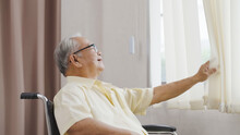 Old Asian Man Sits In A Wheelchair And Looks Out The Window. Health Care And Insurance, Retirement Concept