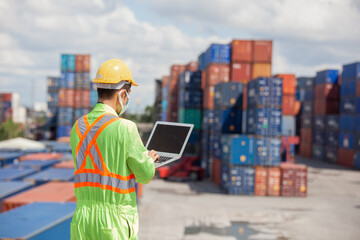 worker standing in shipping container yard holding laptop with smile. Import and export product. Manufacturing transportation and global business concept.