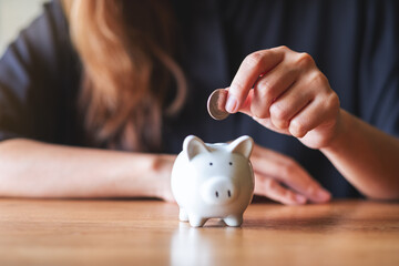 Wall Mural - Closeup image of a woman putting coin into piggy bank for saving money concept