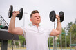 © Евгений Шемякин - handsome serious happy strong athletic man athlete bodybuilder training with dumbbells outdoors at open air gym at summer, gain hands and shoulders muscles. Bodybuilding fitness, healthy lifestyle