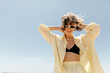 Stylish adorable pretty woman with wavy hair wearing linen yellow suit in sunglasses dancing and having fun against blue sky in summer sunny day 
