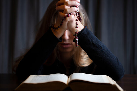 Christianity theme – prayer.  Christian woman with Bible praying with hands crossed keeping rosary.