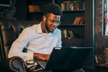 Businessman with laptop. Cheerful young African businessman typing something on laptop