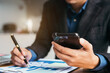 © NINENII - Male writes information businessman working on smartphone writing business plan while sitting in office.