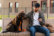 © NFstock - Waist up portrait view of the caucasian man looking at his dog attentively and stroking him while sitting together at the street. Pet owners concept