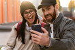 © NFstock - Loving bearded man hugging his wife in the street at the bench while smiling and looking at the smartphone during the making selfie. Caucasian couple in love walking together