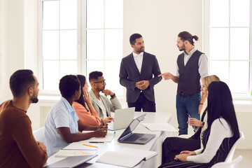 Mixed race group of serious employees sitting around office table during meeting in boardroom and listening to angry team manager criticizing marketing strategy or business project plan they prepared