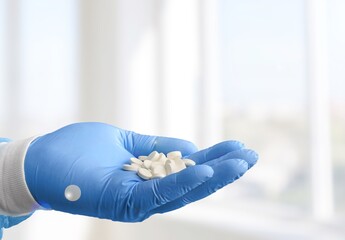 Wall Mural - A medical worker or pharmacist hands wearing blue latex protective gloves, pouring white medicine pills