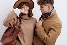 A Close Horizontal Photo Of A Beautiful, Stylish Couple In Autumn Clothes. A Woman Is Wearing A Hat And Holding A Bag On Her Shoulder, And A Man Is Looking At Her