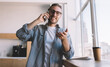 © BullRun - Cheerful man in optical spectacles smiling at camera while making positive mobile conversation, happy millennial hipster guy in classic eyeglasses enjoying friendly communication via cellphone