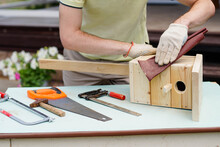 Craftsman Making A Wooden Birdhouse With Tools. DIY Concept. Carpenter Polishing Nesting Box With Sandpaper.