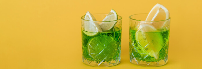 Wall Mural - sliced citrus fruits in glasses with sparkling mojito drink on yellow, banner.