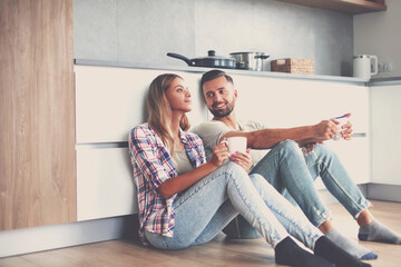 Wall Mural - young couple drinking coffee sitting on the kitchen floor