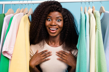 Canvas Print - Photo of positive pretty person arm touch chest stand between clothes rack isolated on blue color background