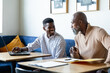 © WavebreakMediaMicro - Smiling african american businessmen discussing over laptop at desk in creative office